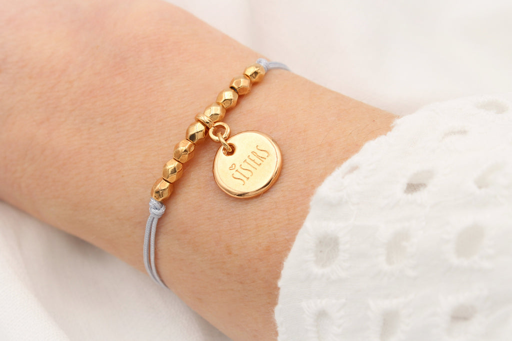 Sisters Armband in hell grau mit rosegoldfarbenem Anhänger am Handgelenk getragen