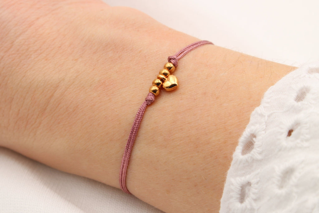 Altrosa Makramee Armband mit kleinem Herz Anhänger und 4 Perlen roségold am Handgelenk der Dame getragen