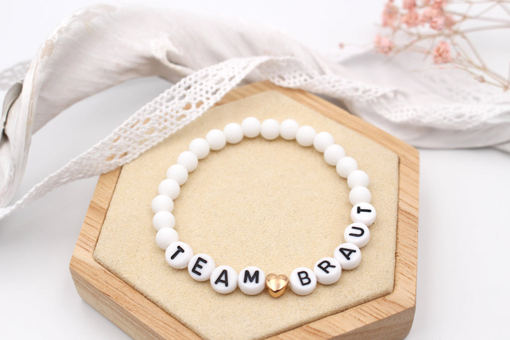 weißes Team Braut Perlenarmband für deinen JGA mit rosegoldfarbenem Herzen auf Holz
