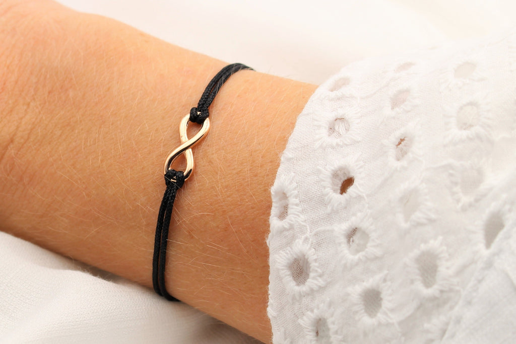 Unendlichkeitsarmband in rosegold mit schwarzem Makrameeband am Handgelenk getragen