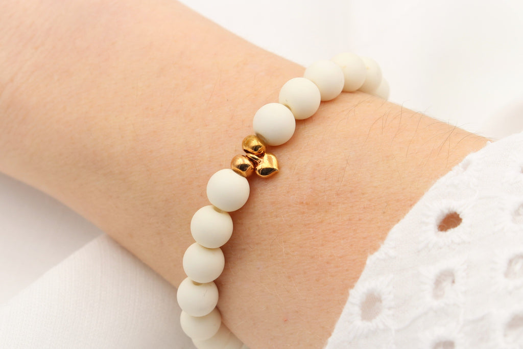 modernes creme mattes Armband aus Pelren und Herz Anhänger gold am Handgelenk getragen