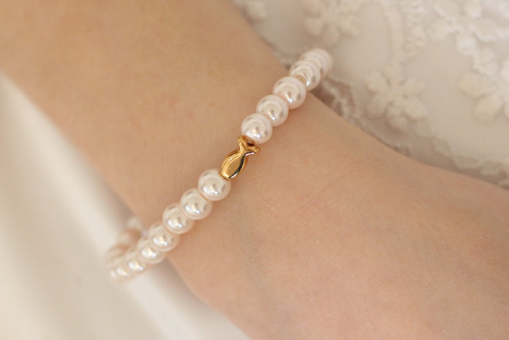 maritimes Perlenarmband in weiß mit Ichthys Fisch in rosegold am Handgelenk des Mädchens getragen