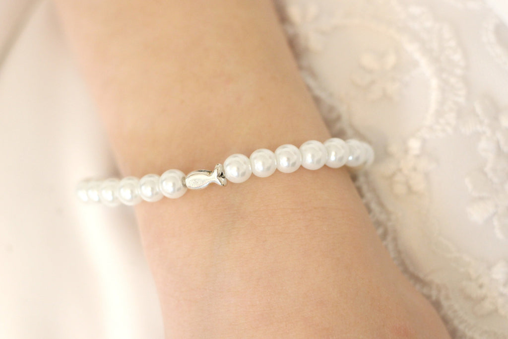 weißes Perlenarmband mit Ichthys Fisch als Symbol am Handgelenk des Kommunion Mädchen getragen