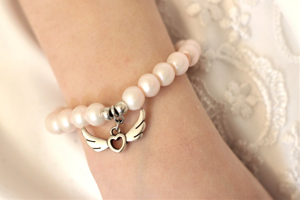 rosa Armband Kommunion mit Anhänger Engelsflügel in silber am Handgelenk des Mädchens getragen