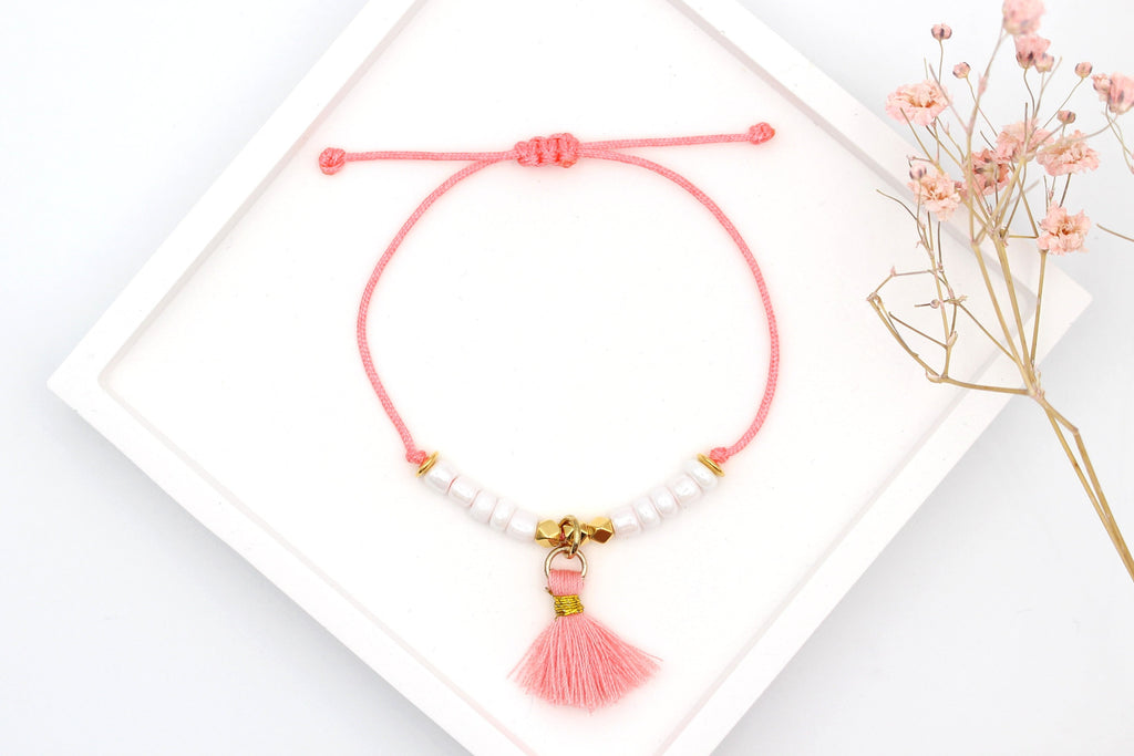 Koralle orange farbenes Makramee Armband mit weißen und goldenen Perlen sowie einer kleinen Quaste als Anhänger und geflochtenem Verschluss