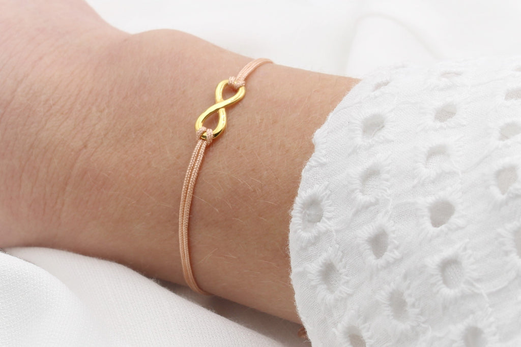pfirsich farbenes Damen Makramee Armand mit goldenem Infinity Zeichen am Hangelenk getragen