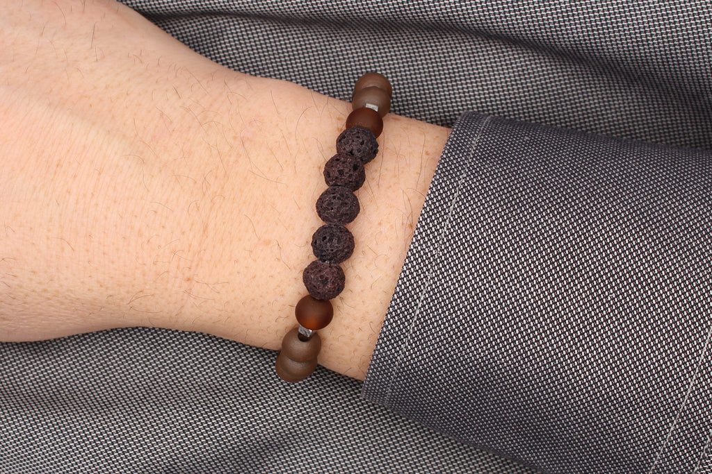 Herrenarmband aus braun schwarzen Perlen mit silberfarbigen Details am Handgelenk des Mannes getragen