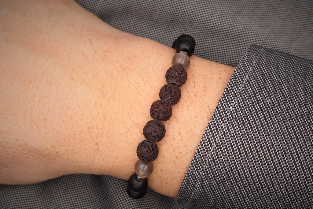 Herrenarmband aus schwarzen Lavaperlen und Holzperlen mit grauen Details am Handgelenk des Mannes getragen als Geschenkidee zum Vatertag